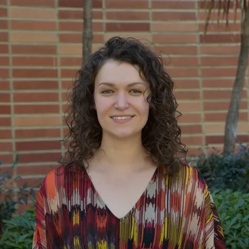 Headshot of Ivanna Evans - person smiling in front of greenery and a brick wall