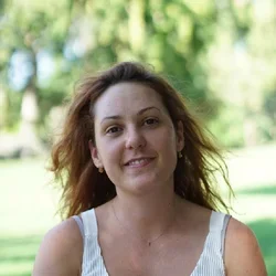 Headshot: a person smiling in front of a leafy background